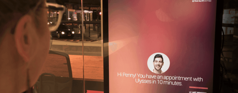 A visitor looking at the SophieHub display, which reads 'Hi Penny! You have an appointment with Ulysses in 10 minutes.'